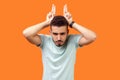 Portrait of angry bully brunette man showing bull horn gesture. indoor studio shot isolated on orange background Royalty Free Stock Photo