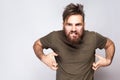Portrait of angry crazy bearded man with dark green t shirt against light gray background.
