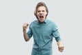 Portrait of angry crazy handsome long haired blonde young man in blue casual shirt standing, looking at camera, screaming and Royalty Free Stock Photo