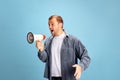 Portrait of angry crazy wild young man shouting to loudspeaker isolated blue studio background. Irritated young guy in