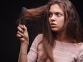 Woman brushing tangled hair with a comb on a black background. Girl looking at damaged sick hair. Hair problems concept. Royalty Free Stock Photo