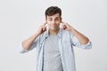 Portrait of angry and frustrated handsome man in blue shirt stopping his ears, plugging them with fingers, pursing lips