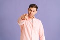 Portrait of angry handsome young man pointing index finger at you on purple  background, looking at camera. Royalty Free Stock Photo