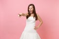 Portrait of angry irritated bride woman in white wedding dress swearing screaming pointing index finger aside isolated