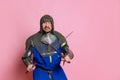 Portrait of angry man, medieval warrior or knight in special armor crossing swords isolated over pink studio background Royalty Free Stock Photo