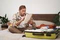 Portrait of angry man, packing suitcase, looking frustrated at notebook with check list of items for holiday, preparing Royalty Free Stock Photo