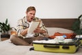 Portrait of angry man, packing suitcase, looking frustrated at notebook with check list of items for holiday, preparing Royalty Free Stock Photo