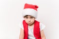 Portrait of angry resentful little child in red Santa Claus hat isolated on white background. Beautiful 5 year European boy.