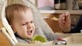 Portrait of angry screaming baby boy refusing eating food while sitting in highchair Royalty Free Stock Photo