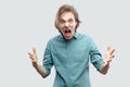 Portrait of angry screaming handsome long haired blonde young man in blue casual shirt standing with raised arms, aggressive Royalty Free Stock Photo