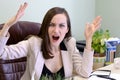 Portrait of angry, screaming young business woman in a leather chair behind the office Desk Royalty Free Stock Photo