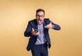 Portrait of angry stressed male manager pointing at mobile phone and shouting furiously against yellow background. Frustrated Royalty Free Stock Photo