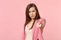 Portrait of angry strict young woman wearing jacket pointing index finger on camera isolated on pastel pink wall