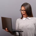 Portrait of angry woman screaming at her laptop against gray background