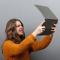 Portrait of angry woman screaming at  her laptop against gray background Royalty Free Stock Photo