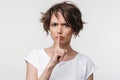 Portrait of angry woman with short brown hair in basic t-shirt holding index finger on lips Royalty Free Stock Photo