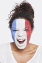 Portrait of angry young African American woman with French flag painted on face shouting against white background Royalty Free Stock Photo