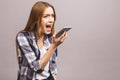 Portrait of an angry young woman shouting at a mobile phone, isolated on a grey background Royalty Free Stock Photo
