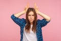 Portrait of angry young woman showing bull horn gesture, looking at camera with hostile menace expression Royalty Free Stock Photo