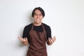 Portrait of annoyed Asian barista man in brown apron making angry hand gesture with fingers Royalty Free Stock Photo