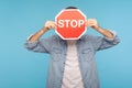Portrait of anonymous man in worker denim shirt covering face with Stop road traffic sign as symbol of prohibition Royalty Free Stock Photo