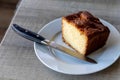 A portrait of a apple pound cake on a white plate on a wooden table with a bread knife on the plate. It is made from apples, sugar