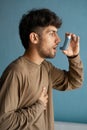 portrait of arabic young man using asthma inhaler against blue background at home