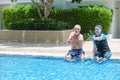 Portrait asia senior woman and caucasian old man resting together in the edge of swimming pool in clubhouse Royalty Free Stock Photo