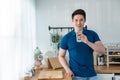 Portrait of Asian attractive male holding a glass of water in kitchen. Young thirsty handsome man pouring and drink clean mineral