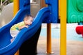 Portrait of an Asian baby boy seriously trying to climb blue slide, Toddler playing with toy amidst an outdoor playground. Royalty Free Stock Photo