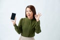 Portrait Asian beautiful happy young woman standing smile, holding mobile phone and showing ok gesture Royalty Free Stock Photo