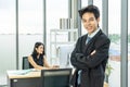 Portrait of asian business man standing in office with her arms crossed with businesswoman working on laptop is background Royalty Free Stock Photo