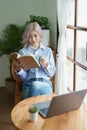 Portrait of an Asian business woman drinking coffee while reading book with a computer on her desk Royalty Free Stock Photo