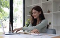 Portrait of asian business woman paying bills online with laptop in office. Beautiful girl with computer and chequebook Royalty Free Stock Photo