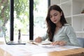 Portrait of asian business woman paying bills online with laptop in office. Beautiful girl with computer and chequebook Royalty Free Stock Photo