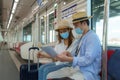 Portrait of Asian couple tourists with mask standing and holding the paper metro map together in the Skytrain in Bangkok, Thailand Royalty Free Stock Photo