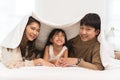 Portrait of Asian family, young mother, father, little cute daughter lying under a duvet or blanket together on bed in bedroom at Royalty Free Stock Photo