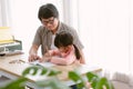 Portrait of Asian father and cute little daughter sitting at table drawing a picture or writing book with colour pencils at home. Royalty Free Stock Photo