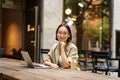 Portrait of asian girl in glasses, sitting with laptop in cafe, working remotely, studying online, posing with coffee