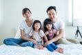 Portrait of Asian happy family smile and look at camera on bed at home. Loving couple and young little girl sibling daughters