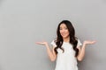 Portrait of asian indecisive woman with dark curly hair shrugging and throwing hands aside with clueless, isolated over gray back Royalty Free Stock Photo