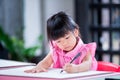 Portrait Asian kid sitting on large sheet of drawing paper on table. Students concentrate on art work. 4 year old girl wears pink Royalty Free Stock Photo