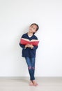 Portrait asian little child girl in casual school uniform reading a book and standing against white wall in the room Royalty Free Stock Photo