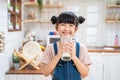 Portrait of Asian little cute kid holding a cup of milk in kitchen in house. Young preschool child girl or daughter stay home with