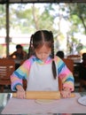 Portrait of asian little girl using wooden rolling pin on Dough for pizza. Homemade process of preparation pizza