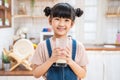 Portrait of Asian little kid holding a cup of milk in kitchen at home. Young preschool cute child girl or daughter stay home with