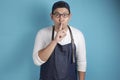 Portrait of Asian male chef or waiter put finger on his mouth, ask to be silent, keep secret gesture