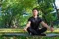 Portrait of Asian man in autumn park meditating sitting in lotus position on fitness mat, sportsman resting after Royalty Free Stock Photo