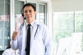 Asian man doctor with headset and stethoscope, thumbs up standing with computer to advice medicines or medical treatment Royalty Free Stock Photo