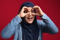 Portrait of Asian muslim woman looking to camera, smiling while looking or peeking through her fingers over red Royalty Free Stock Photo